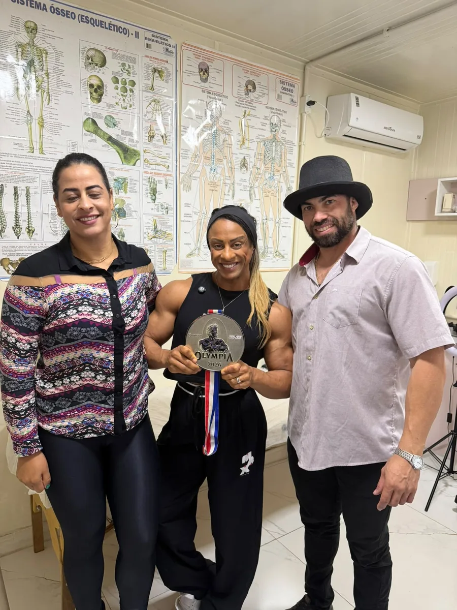 Atleta com a medalha de vice-campeã do Miss Olympia 2026, ao lado do Dr. Jonas e da Marlize